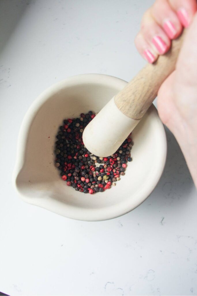 Hand using a pestle and mortar to crush black peppercorns.