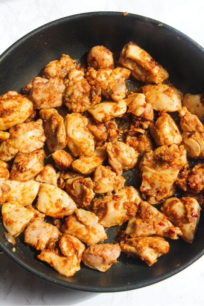 Diced chicken coated in spices in a smal frying pan.