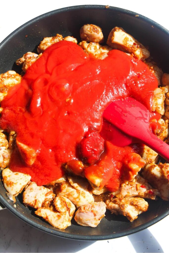 Tomato passata poured over cooked chicken in a small frying pan.