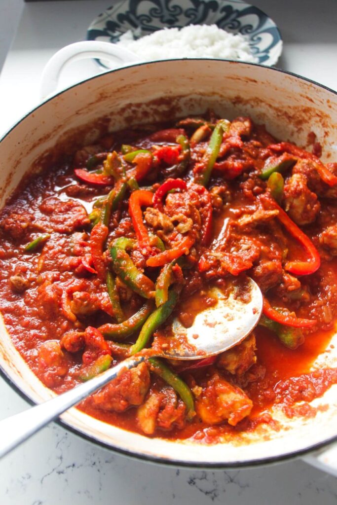 Chicken jalfrezi curry in a large pan with a spoon.
