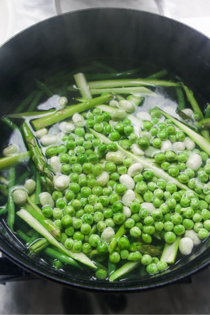 Peas, edamame beans, green beans and asparagus in a large pot of water.