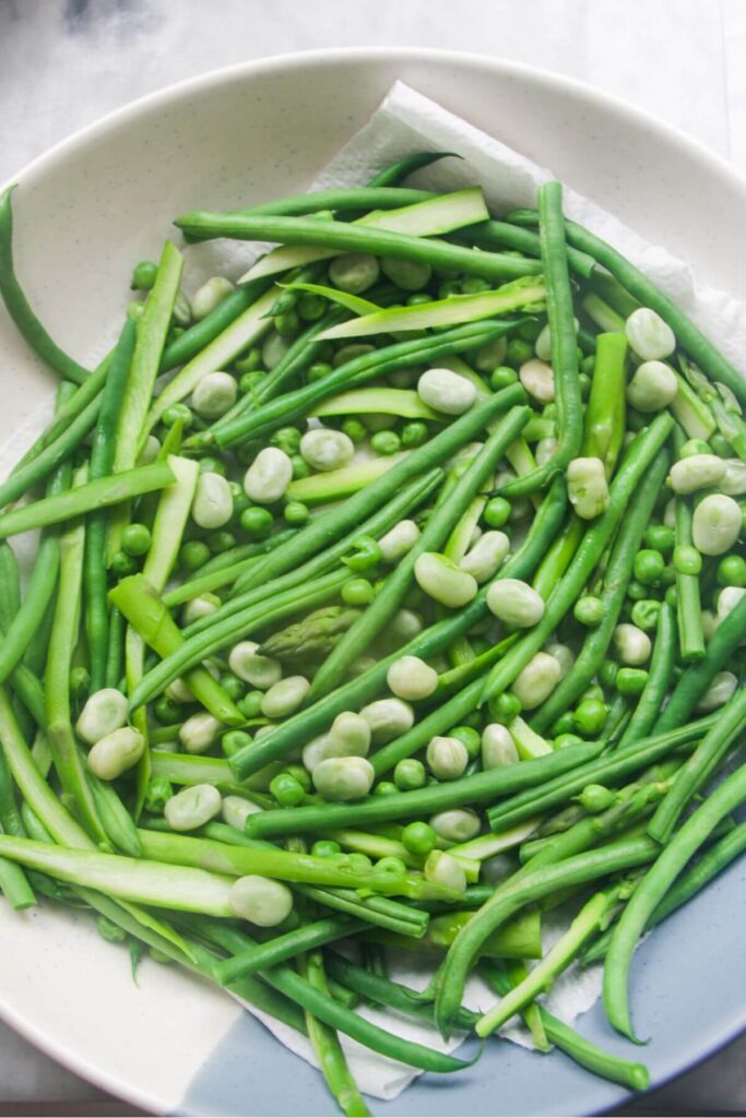 Green beans, asparagus, edamame beans and peas draining in a large serving bowl.