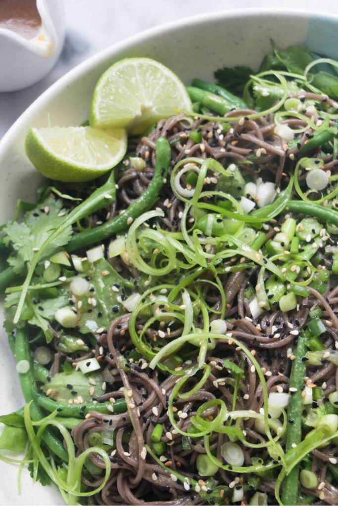 Close up view of soba noodle salad with lots of green vegetables in it.